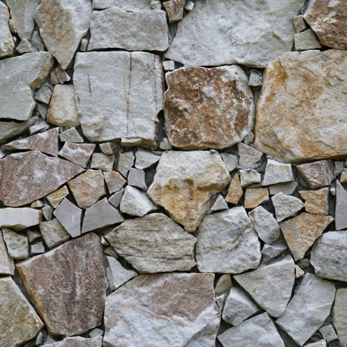 Nahaufnahme einer Natursteinmauer mit unregelmäßigen Mustern aus beigen und grauen Steinen unterschiedlicher Größe.